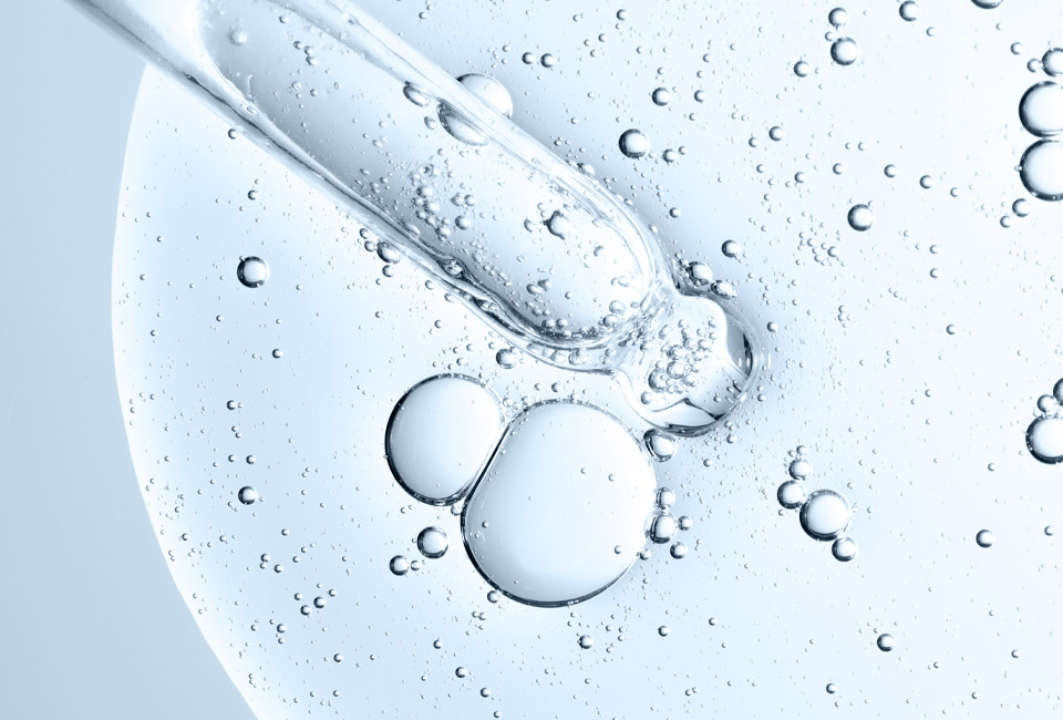 Top-down view of a glass cosmetic dropper over clear liquid with bubbles.